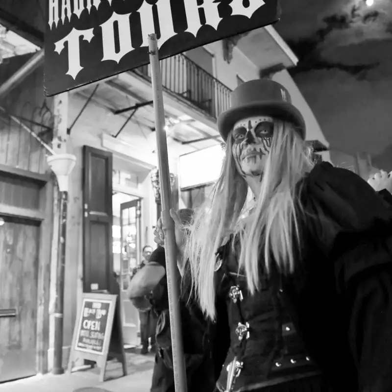 Person in Gothic makeup holds 'Haunted History Tours' sign at night on a city street.